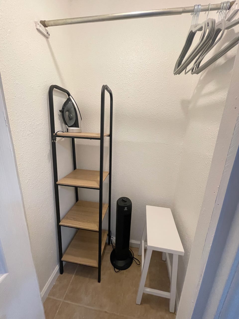 Closet with additional shelving for storage, a stand alone fan & an iron.