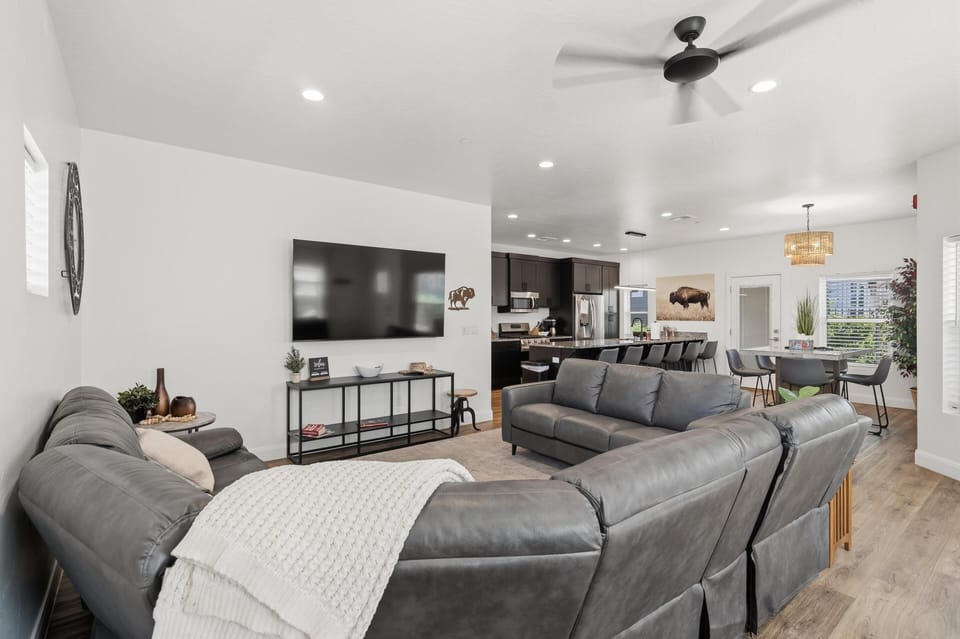 Gray leather sectional faces a wall-mounted TV, with black kitchen cabinets and dining area in view.