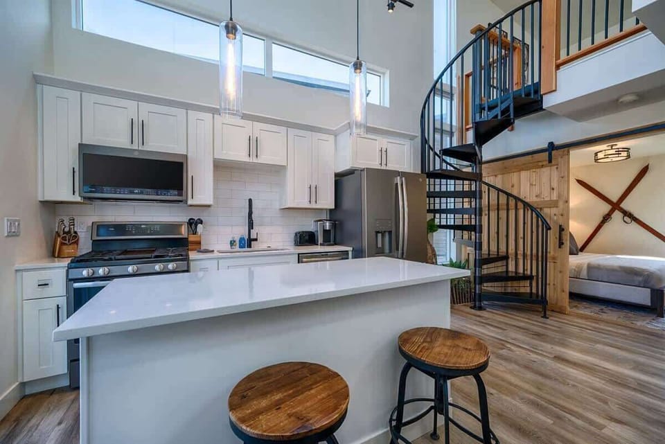 The space features a fully equipped kitchen, with bar stools and a countertop on the main floor, with stairs leading up to a loft area.