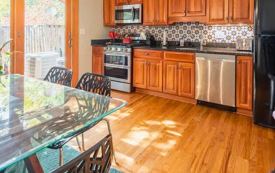 Enjoy meals in this stylish kitchen featuring stainless steel appliances, hardwood floors, and a spacious glass dining table.
