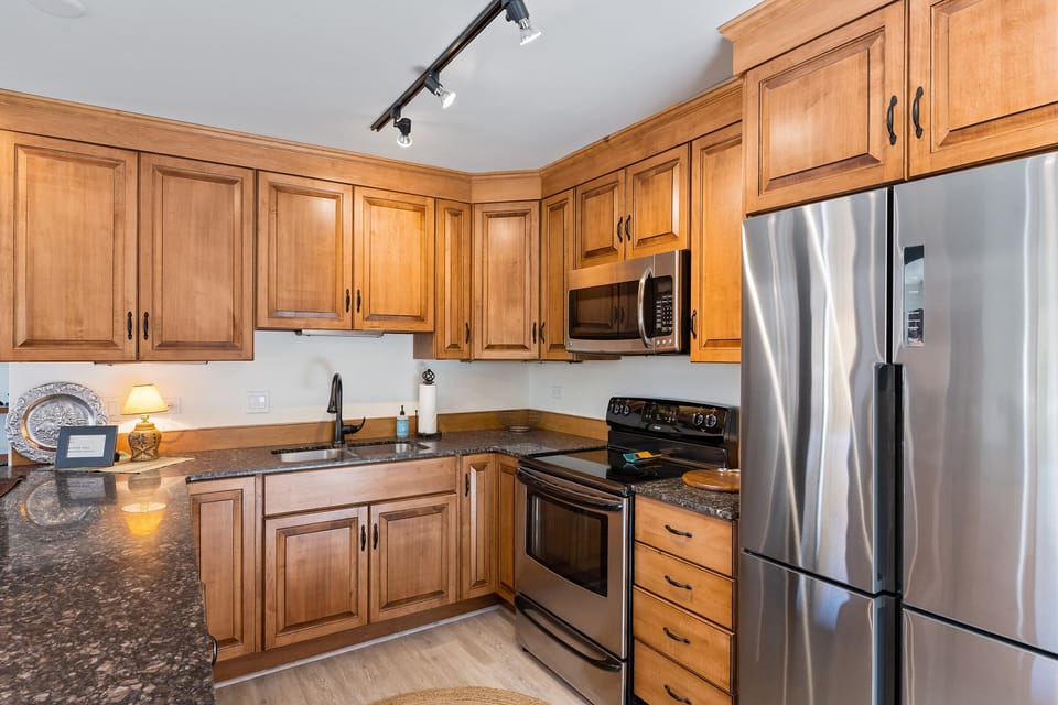 U-shaped kitchen layout with stainless steel fridge, microwave, sink, oven, and granite countertops.