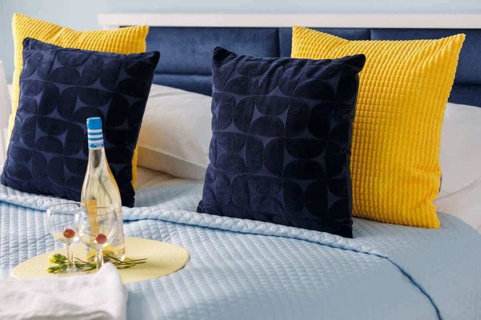 A detailed view of the bed with bright yellow and navy blue pillows, paired with a bottle of sparkling water for a welcoming touch.

