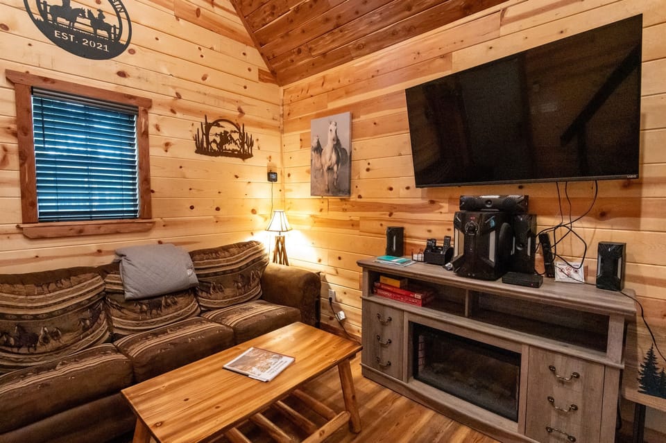 - Warm wood-paneled living room with comfy seating   - Large TV and fireplace add inviting cabin vibes   - Perfect for relaxing after forest adventures
