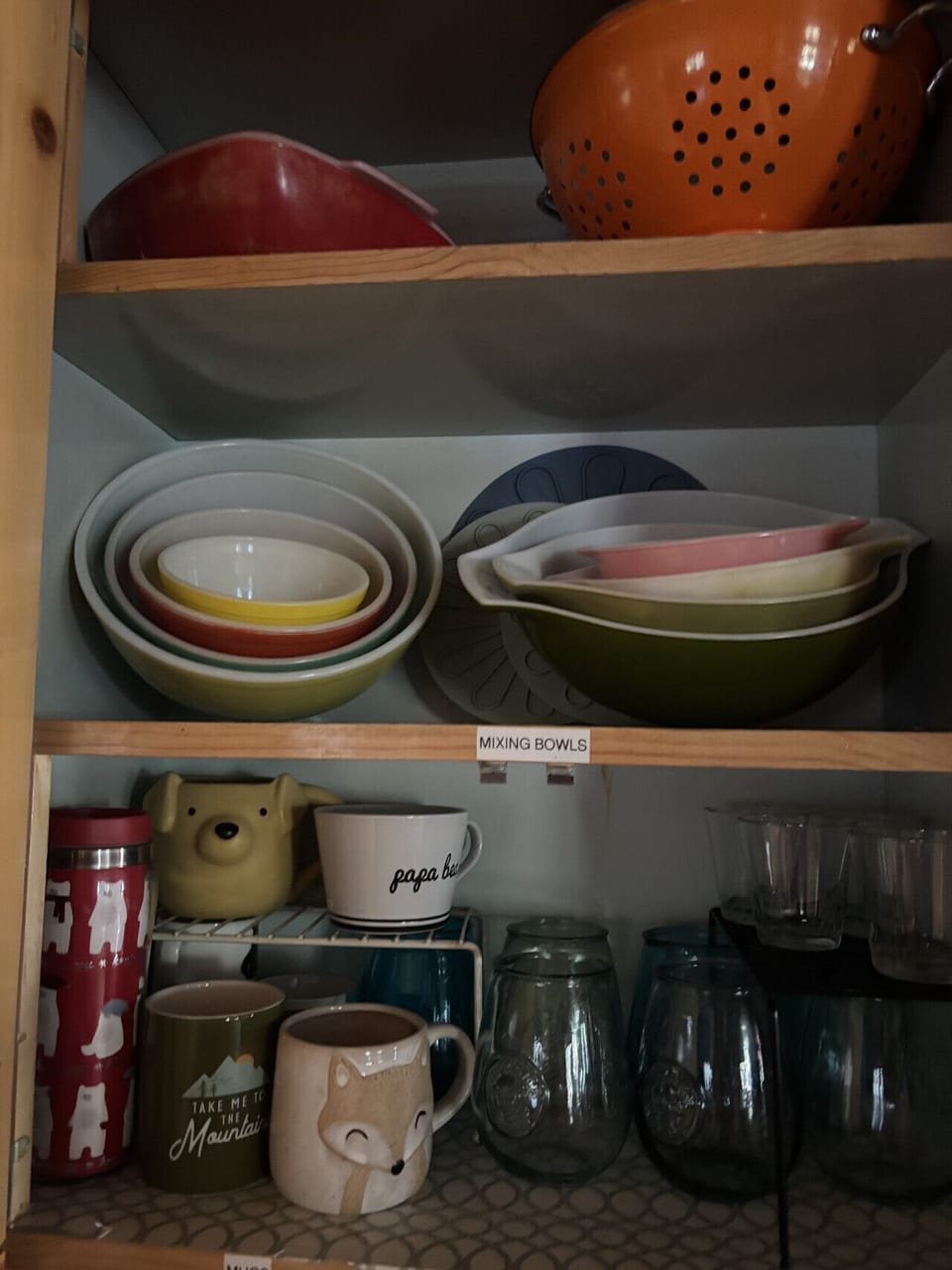 Well-stocked kitchen cabinet featuring colorful mixing bowls, charming mugs, and glassware—everything you need to enjoy home-cooked meals during your stay.