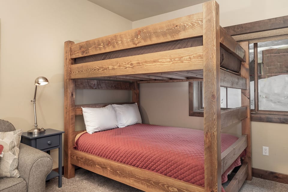 Cozy up in your rustic wooden bunk bed with soft linens and warm coral quilting, perfect for restful nights.