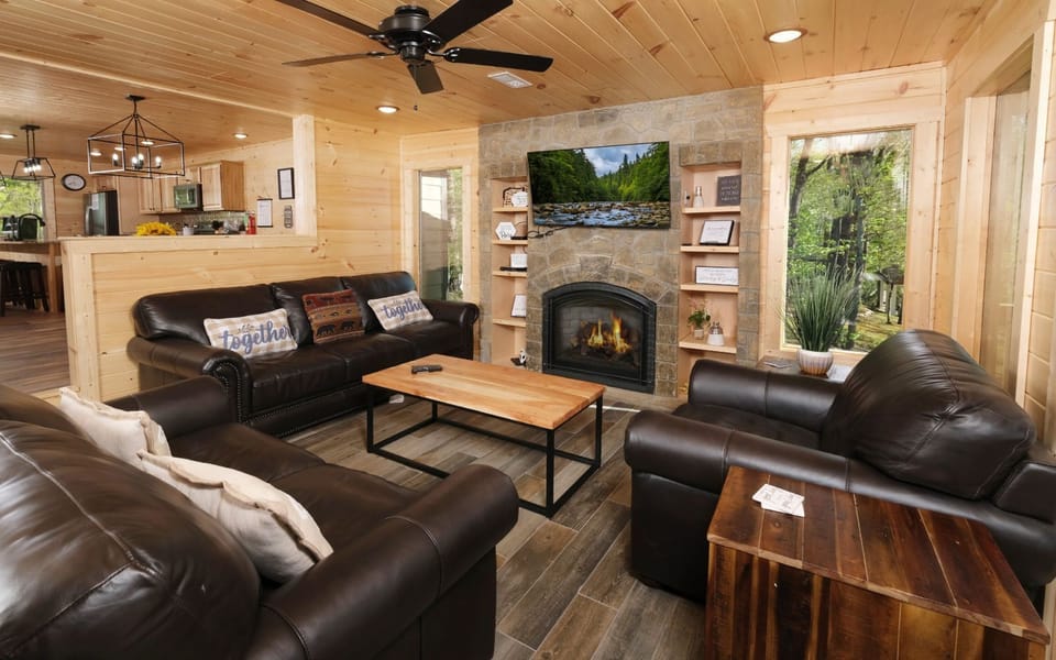 Open concept living area with fireplace, leather sofas, and kitchen view.