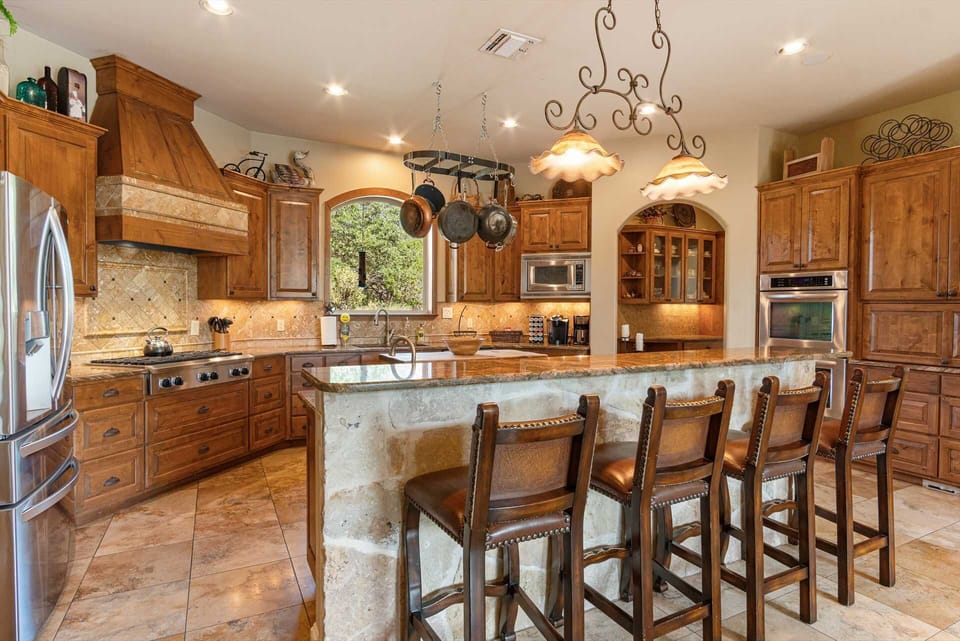 Prepare feasts and gather with loved ones in this expansive gourmet kitchen, boasting rich wooden cabinetry, a large island with bar seating, and state-of-the-art appliances for an unforgettable culinary experience.