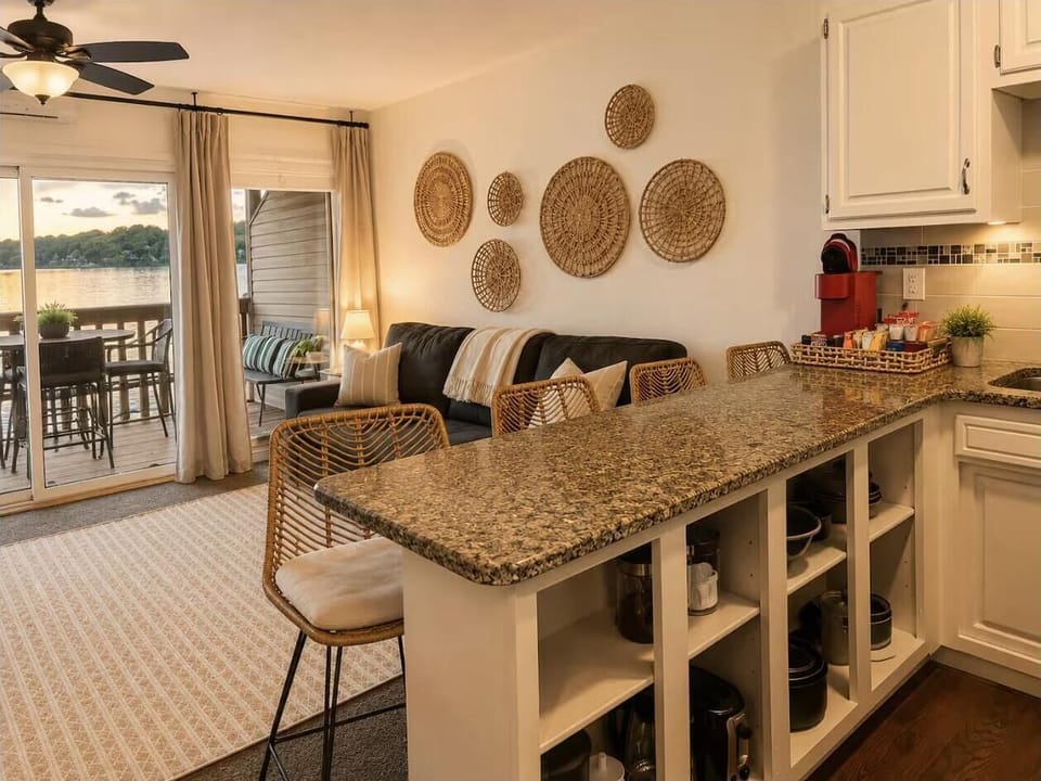 Granite countertop extends into a breakfast bar with stools, overlooking a living room with rattan wall decor.