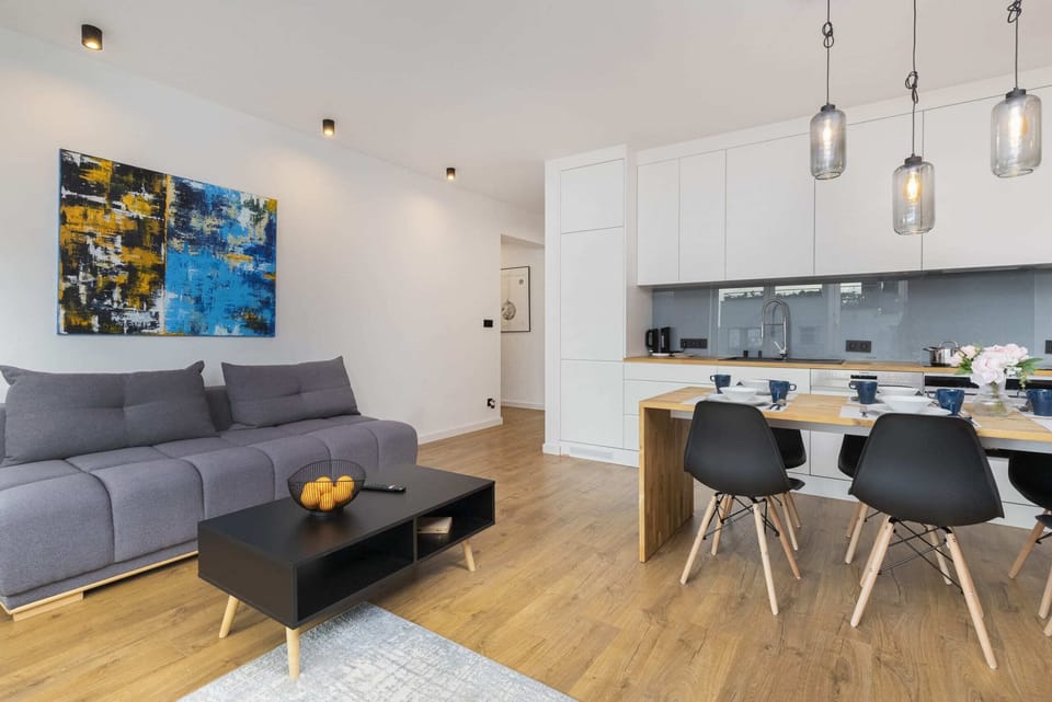 An open-plan space featuring a wooden dining table, black chairs, and a gray sofa in the living area with a bright, modern design.