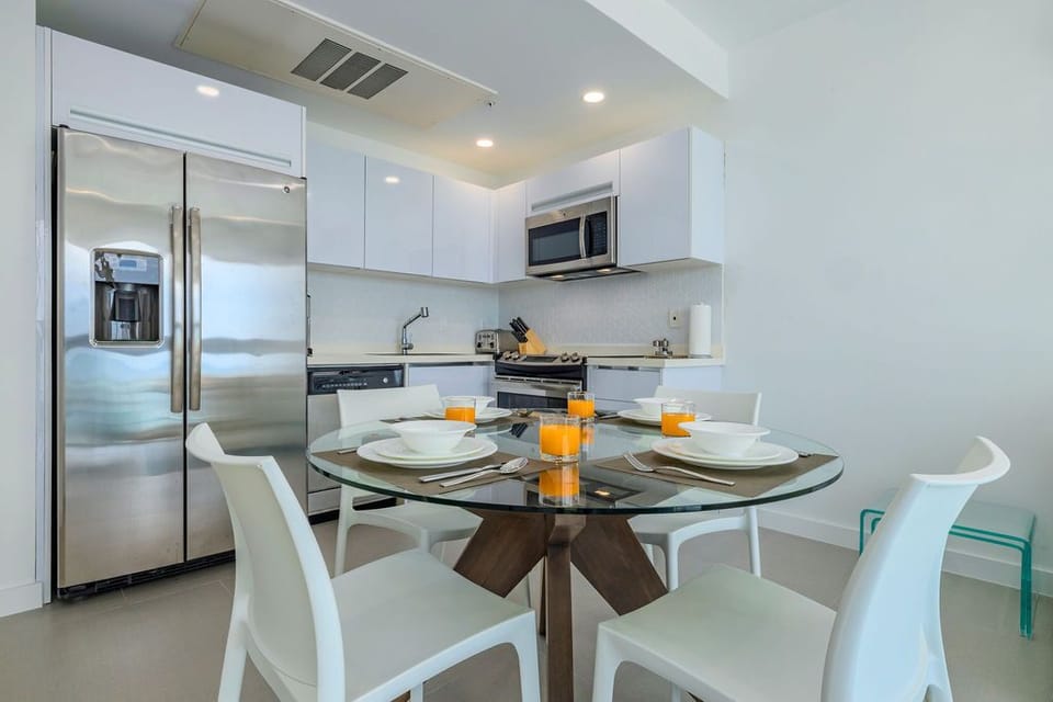 Your sleek, modern kitchen awaits, complete with stainless steel appliances, a stylish glass-top dining table set for four, and all the essentials for preparing and enjoying meals together during your stay.