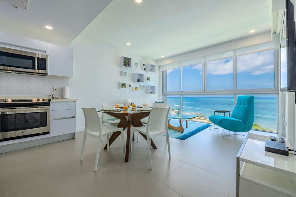 Imagine starting your day at this sleek dining table, sunlight streaming through floor-to-ceiling windows framing stunning ocean views. Your modern kitchen is just steps away, ready for morning coffee or fresh meals.