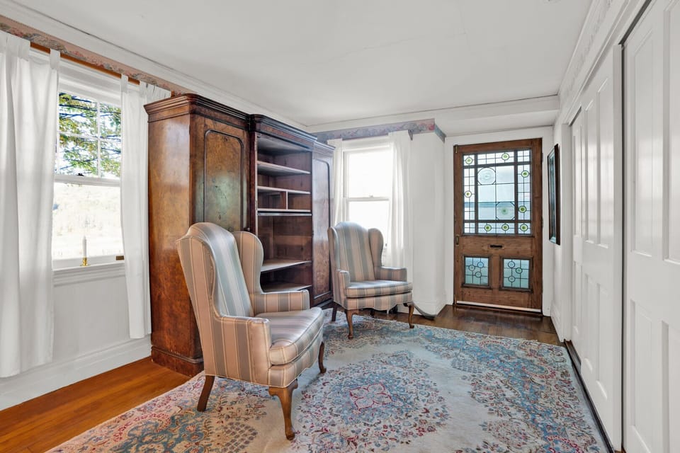 Reading nook with wingback chairs, burlwood armoire, and stained glass door to the porch