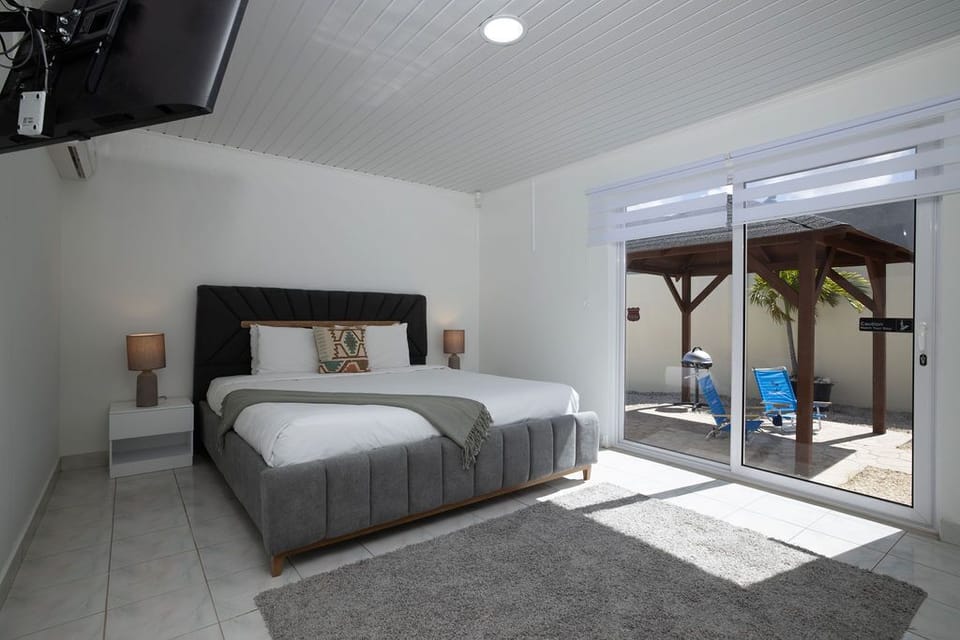 This bedroom features a king-size bed and a comfortable mattress, with a TV, An air conditioning unit, a side table, and lamps. Bright interior and have a WIFI. The sliding door provides access to the BBQ /pool area.