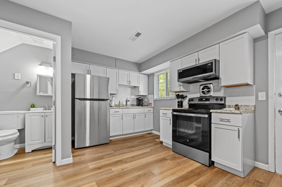 The kitchen includes white shaker cabinets, stone-look counters, a stainless refrigerator, range and microwave, plus a coffee station.