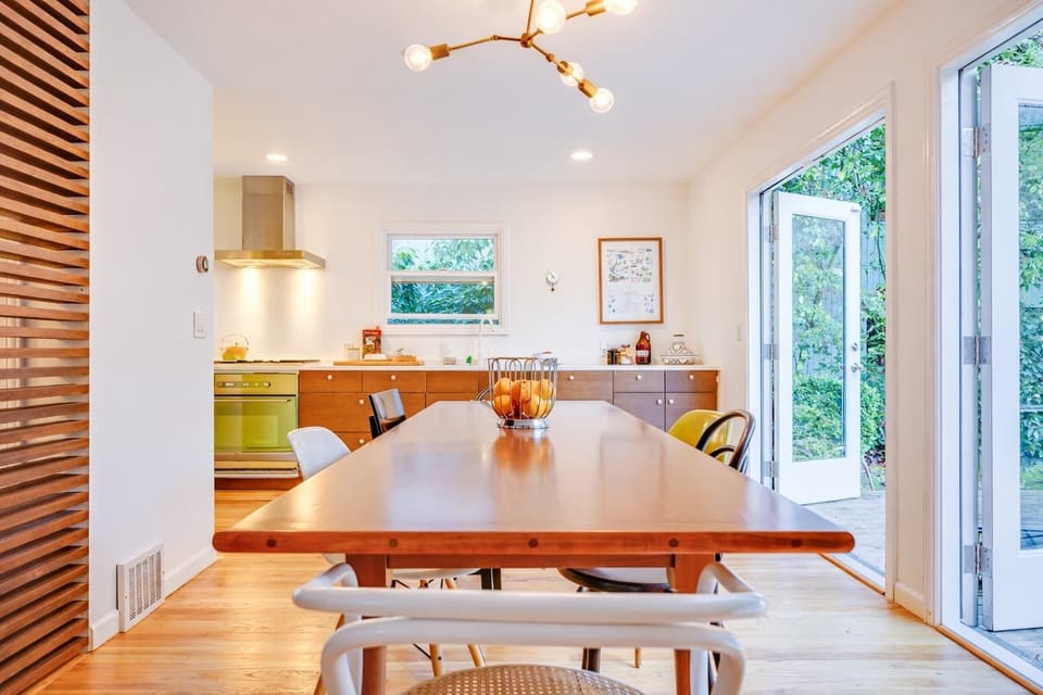 Enjoy meals at this beautiful wooden dining table beside bright windows and garden views, just steps from the modern kitchen.