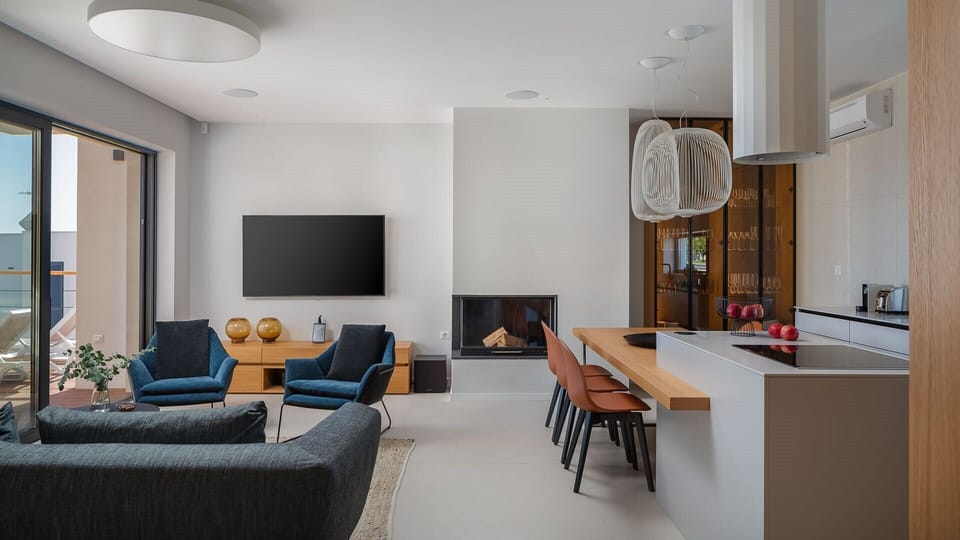 Couch and armchairs in the spacious living room with a fireplace and access to the terrace, and a modern kitchen with kitchen island