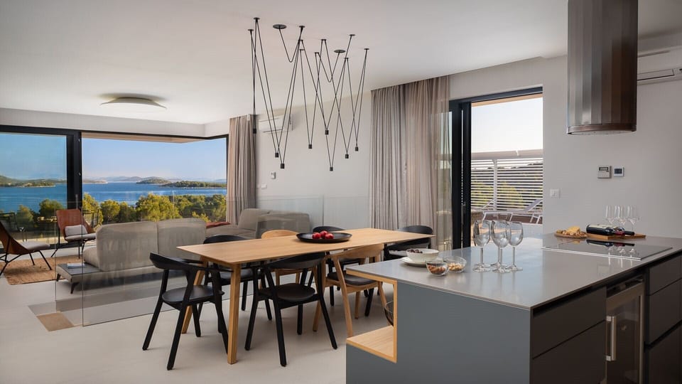 The interior of the living room with a kitchen island, a table for 8 people and sofas of a luxury holiday villa on the island of Murter with a view of the sea