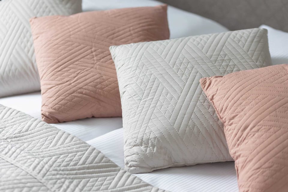 A close-up of decorative pillows in pastel tones placed on the bed.
