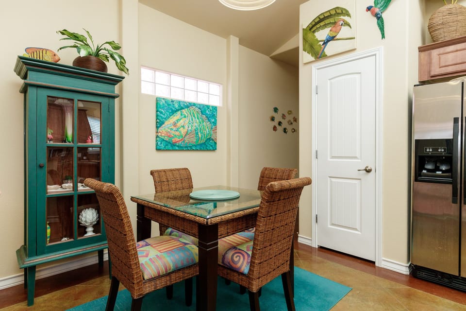 Your tropical-themed dining nook welcomes you with wicker chairs and vibrant artwork, perfect for morning coffee or intimate meals together.