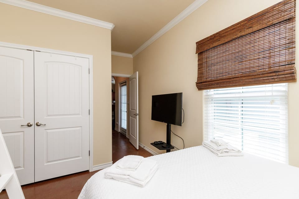 Your peaceful bedroom features a comfortable bed, flat-screen TV, and warm bamboo blinds that filter natural light beautifully.