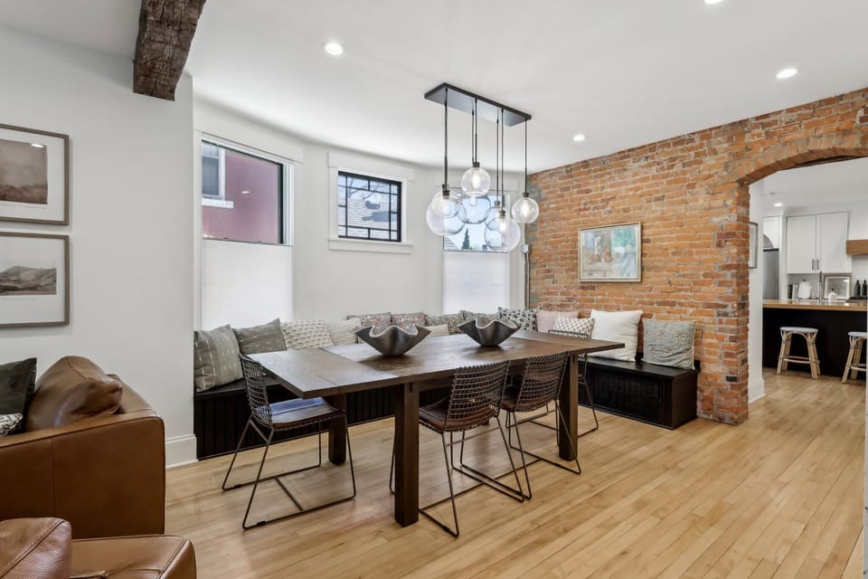 Spacious living room with a stylish table, comfortable chairs, elegant chandelier, and large windows filling the space with natural light for a bright and welcoming atmosphere.