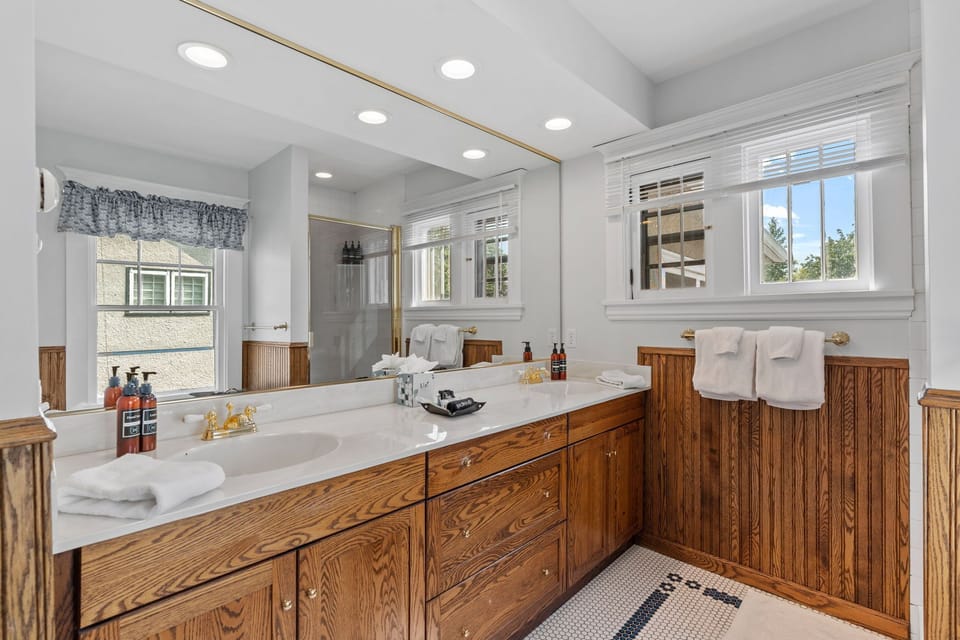 Refresh in this spacious bathroom with luxurious soaking tub, rich wood cabinetry, and bright natural light streaming through plantation shutters.