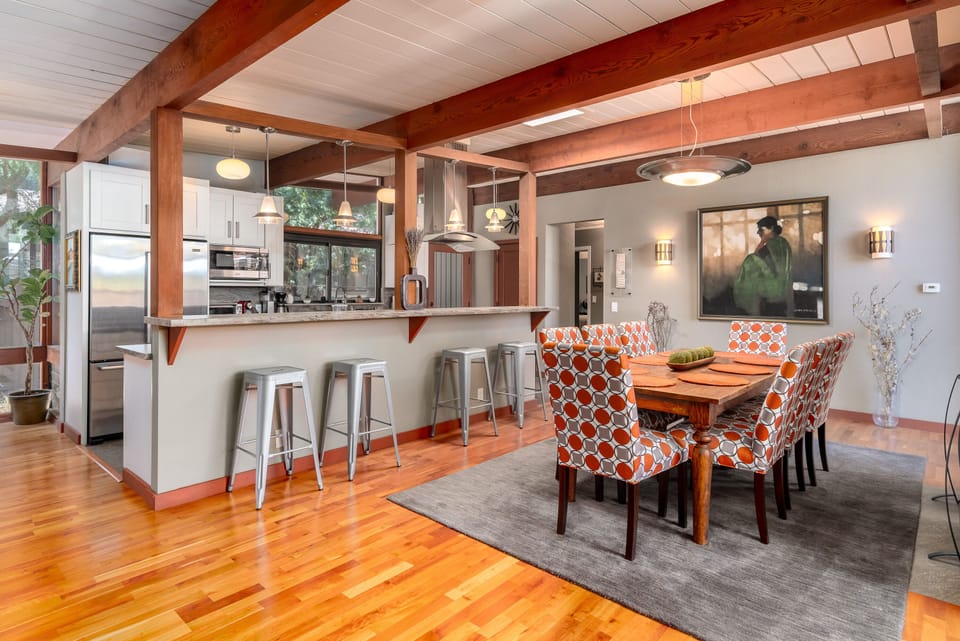 The dining area has a large, elegant dining table with aesthetic chairs and a tasteful rug.  Note the kitchen in the background, with counter stools.