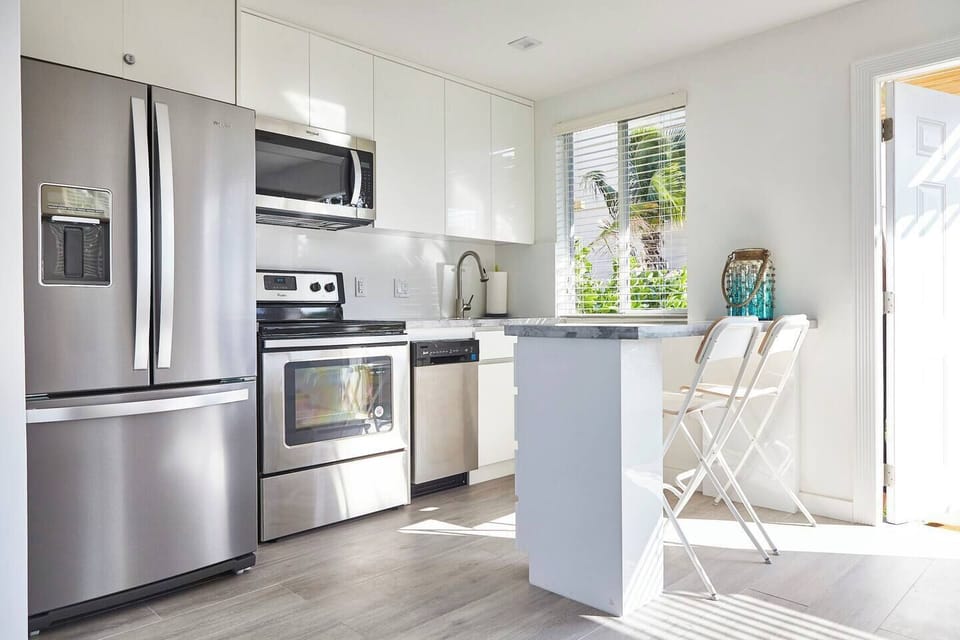 Sleek white kitchen with minimalist design, stainless steel appliances, and marble countertops. Counter can also be used as work space.