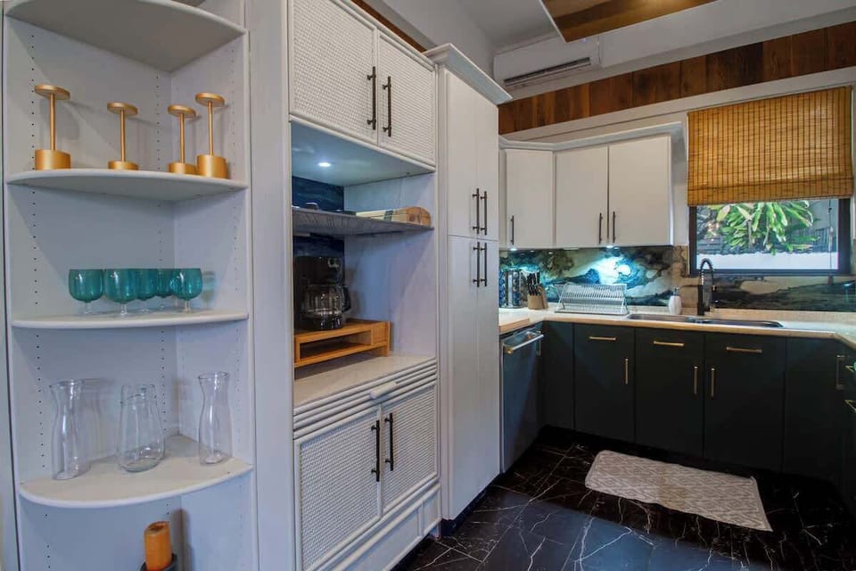 The kitchen features deep blue cabinetry contrasted w/ white upper cabinets & gold hardware. Boasts a unique marble backsplash, complementing the rich wooden accents above. Equipped with modern stainless steel appliances and everything you need.