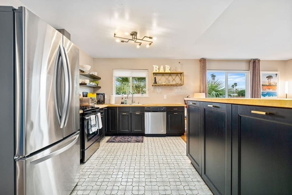 Bright kitchen with dark shaker cabinets, butcher-block counters, stainless appliances & a gold bar shelf — stocked and ready.