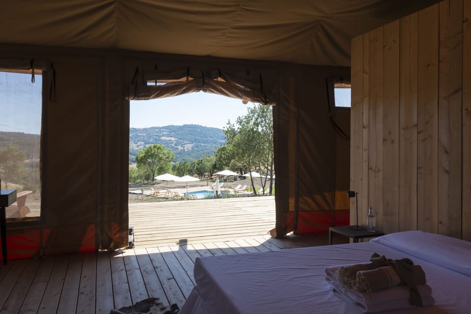 Stardust Lodge interior, spacious and filled with natural light, overlooking the panoramic pool and rolling wilderness hills. Expansive openings create a seamless transition between the indoor space and the deck, where water and landscape merge into one view. Natural wood, soft textiles, and refined details define an atmosphere of exclusive comfort and serenity.