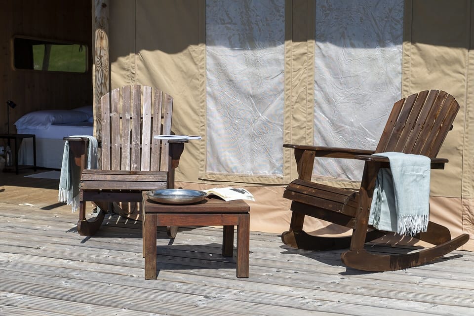 Stardust Lodge outdoor patio defined by rustic elegance and exclusive comfort. Solid wood rocking chairs on the panoramic deck create a private space dedicated to relaxation, surrounded by silence and nature. Natural light, noble materials, and a serene atmosphere shape a refined outdoor living experience within the wilderness.