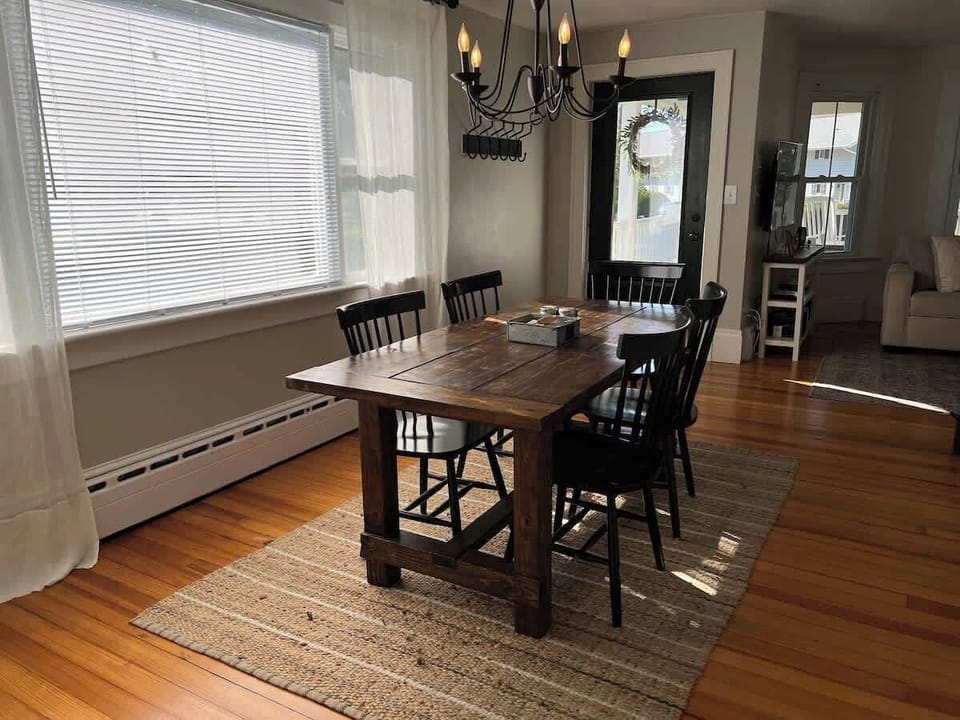 This naturally-lit Dining Area has the beautiful original wood flooring. This open-concept space extends into the Living Room and to the front entrance.  The farmhouse dining table offers  seating for up to six and is adorned with a chandelier.