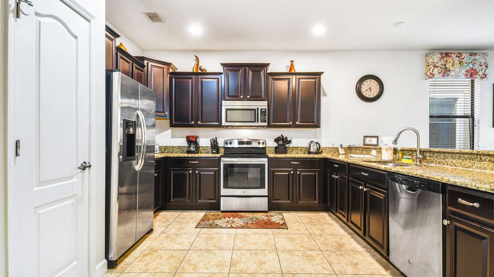 A modern kitchen with dark wood cabinets, granite countertops, stainless steel appliances, and a tiled floor.