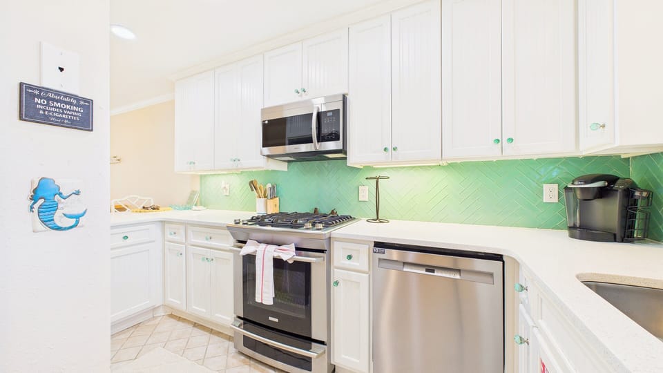 Your bright kitchen features white cabinets, stainless steel appliances, and a cheerful mint green backsplash that adds coastal charm to meal prep.