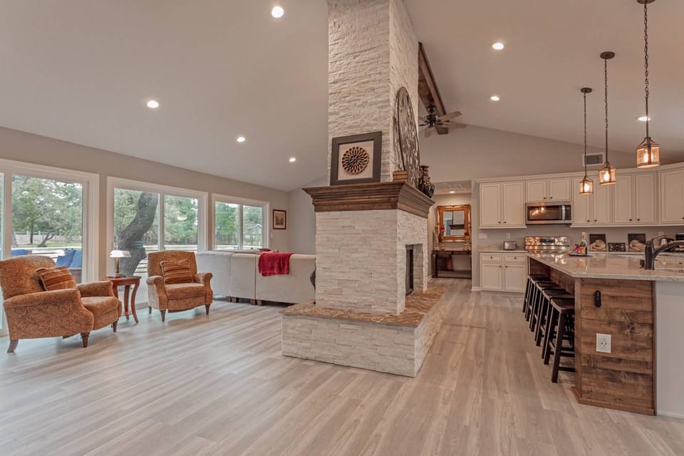 Grand room with floor-to-ceiling fireplace centerpiece, multiple sitting areas, an open kitchen and dining room.