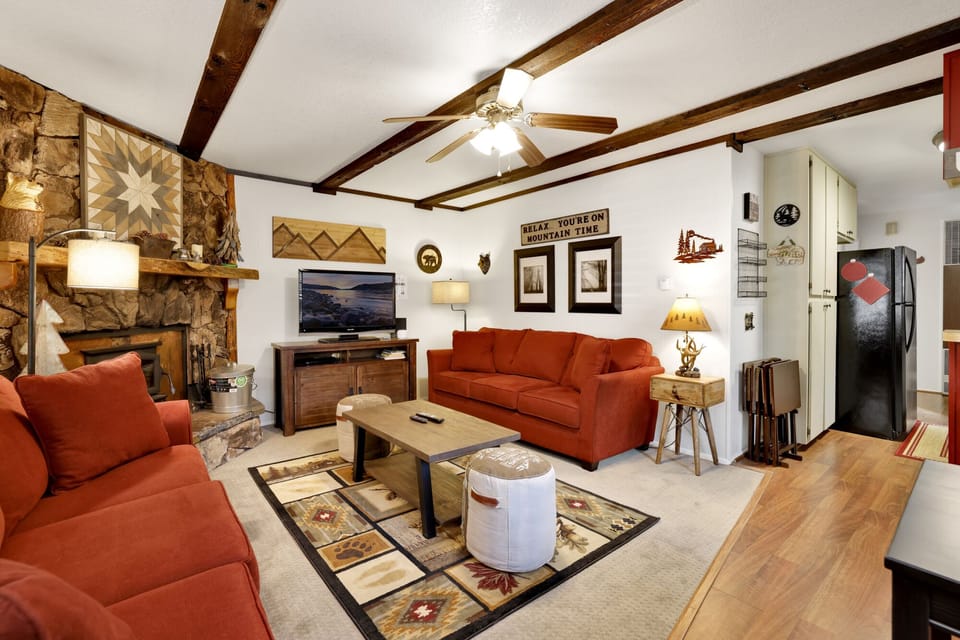 Cozy mountain living room with a stone fireplace, comfy seating, and smart TV—perfect for relaxing evenings, movie nights, and warm cabin vibes after outdoor adventures.