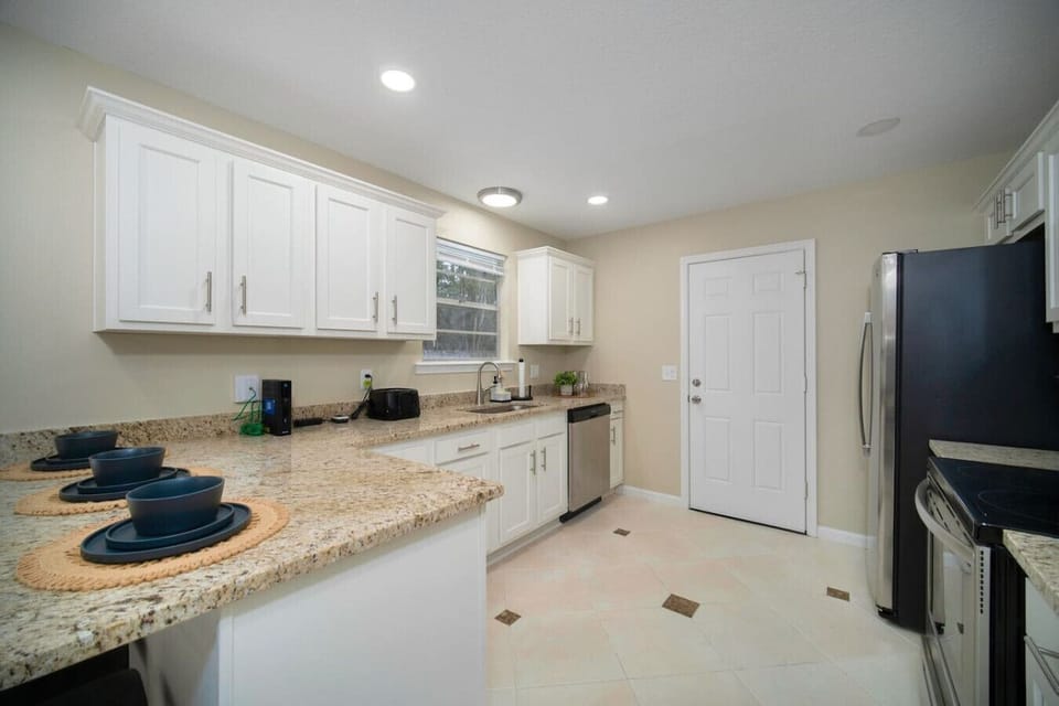 Bright and spacious kitchen featuring modern white cabinetry, a granite countertop, and stainless steel appliances, creating a functional and inviting space.