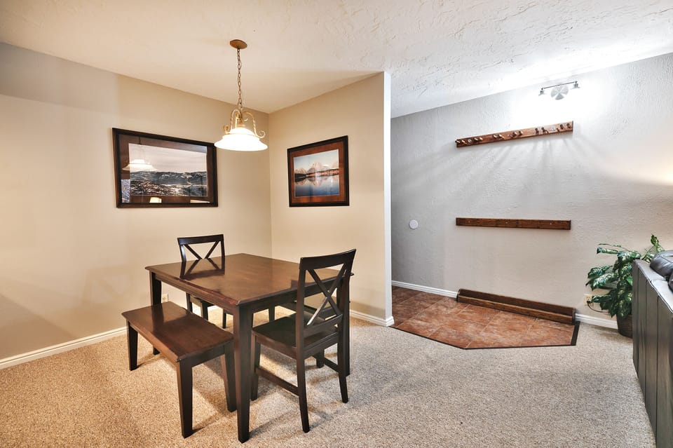 - Dining area with wood table and bench seating  
- Brightly lit space for meals and gatherings  
- Wall art adds mountain charm to cozy condo living