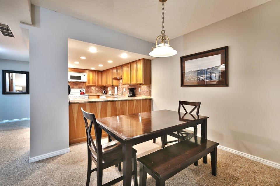 - Dining area beside kitchen with wooden table and bench  
- Warm mountain artwork adds charm to mealtime setting  
- Easy access to fully equipped kitchen for convenience