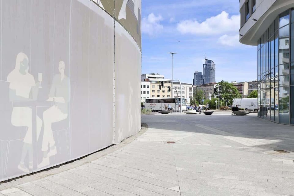 Urban walkway with modern architecture, curved walls, and a view of the city skyline.

