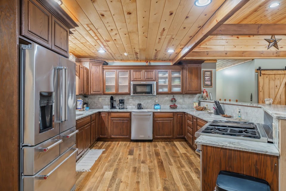 Your fully equipped rustic kitchen welcomes culinary adventures with rich wood cabinetry, gleaming countertops, and modern appliances beneath warm wooden beams.