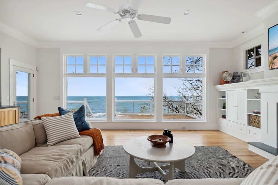 Sink into plush coastal comfort while ocean waves dance beyond your panoramic windows in this bright, airy living space.