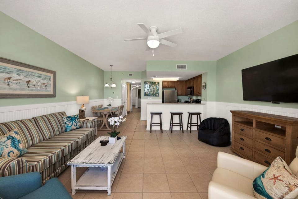 open living area with striped sofa, kitchen bar seating, and a wall-mounted television