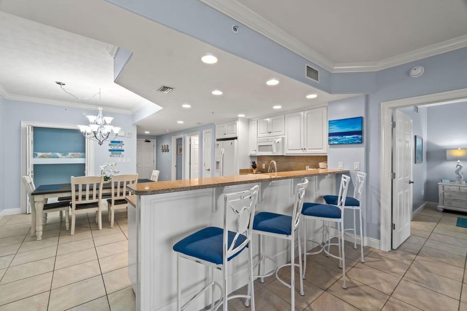 Open kitchen with a breakfast bar and blue cushioned stools overlooking the dining area.
