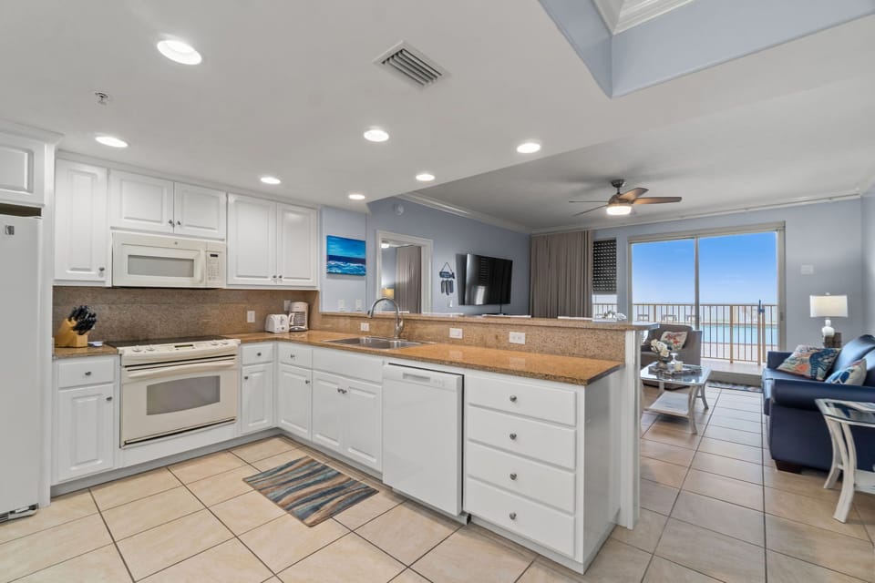 Open kitchen with white cabinetry and a view of the living area and balcony overlooking the water.