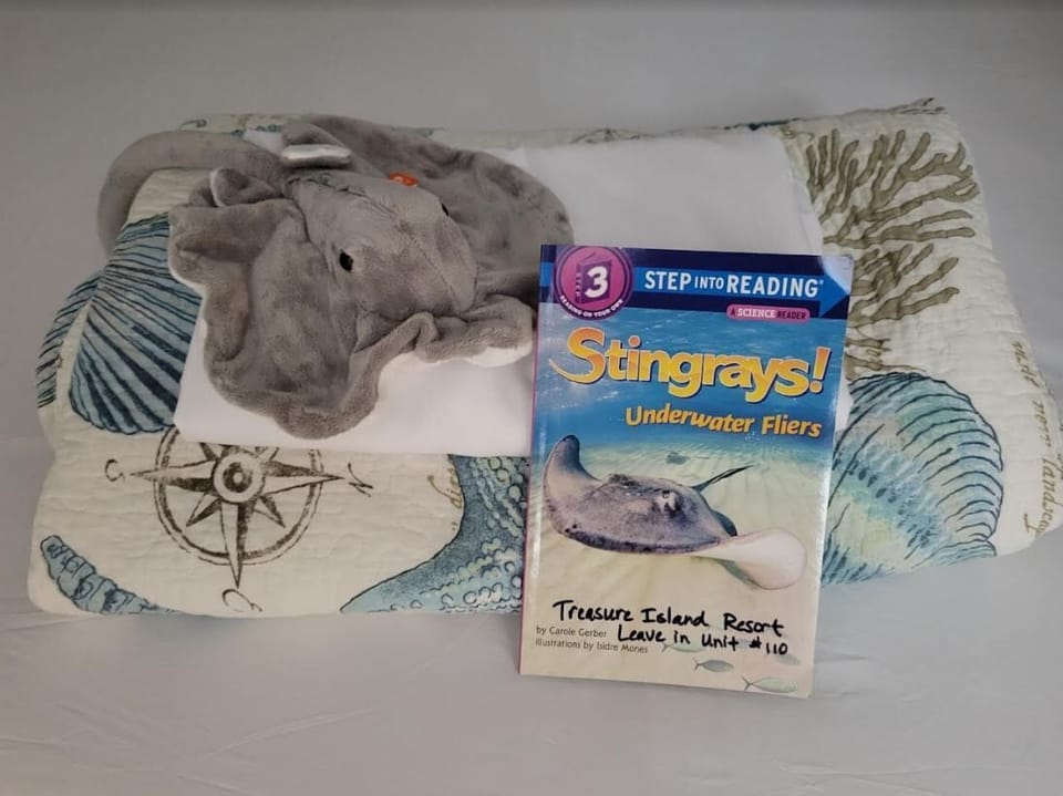 A cozy bed setup with a sea-themed blanket, a plush elephant toy, and a children's book for a family-friendly stay.