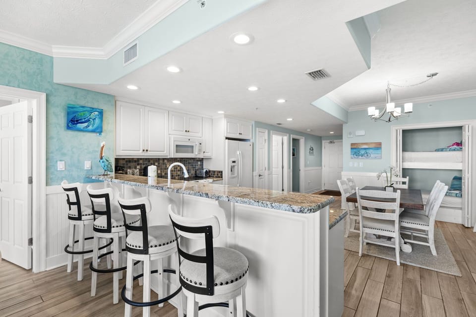 Picture yourself gathering around this coastal-chic kitchen island with room for everyone. The soft blue walls and granite countertop create an easy, beachy vibe perfect for your morning coffee or evening conversations.
