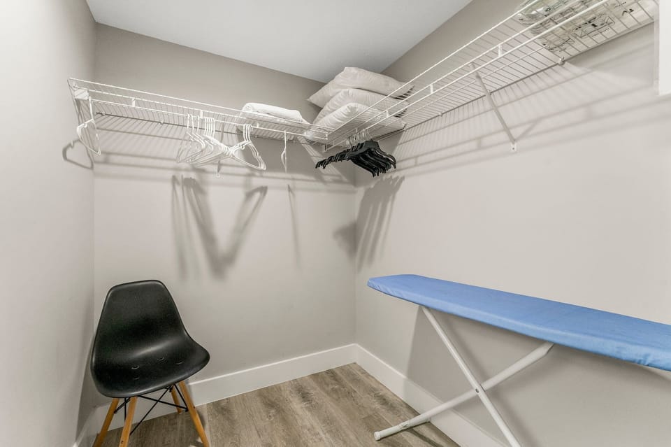 Closet space with wire shelving, hangers, and an ironing board for guest convenience.