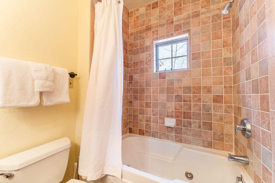 Relax in your private bathroom with beautiful tile work, fresh towels, and natural light streaming through the window.